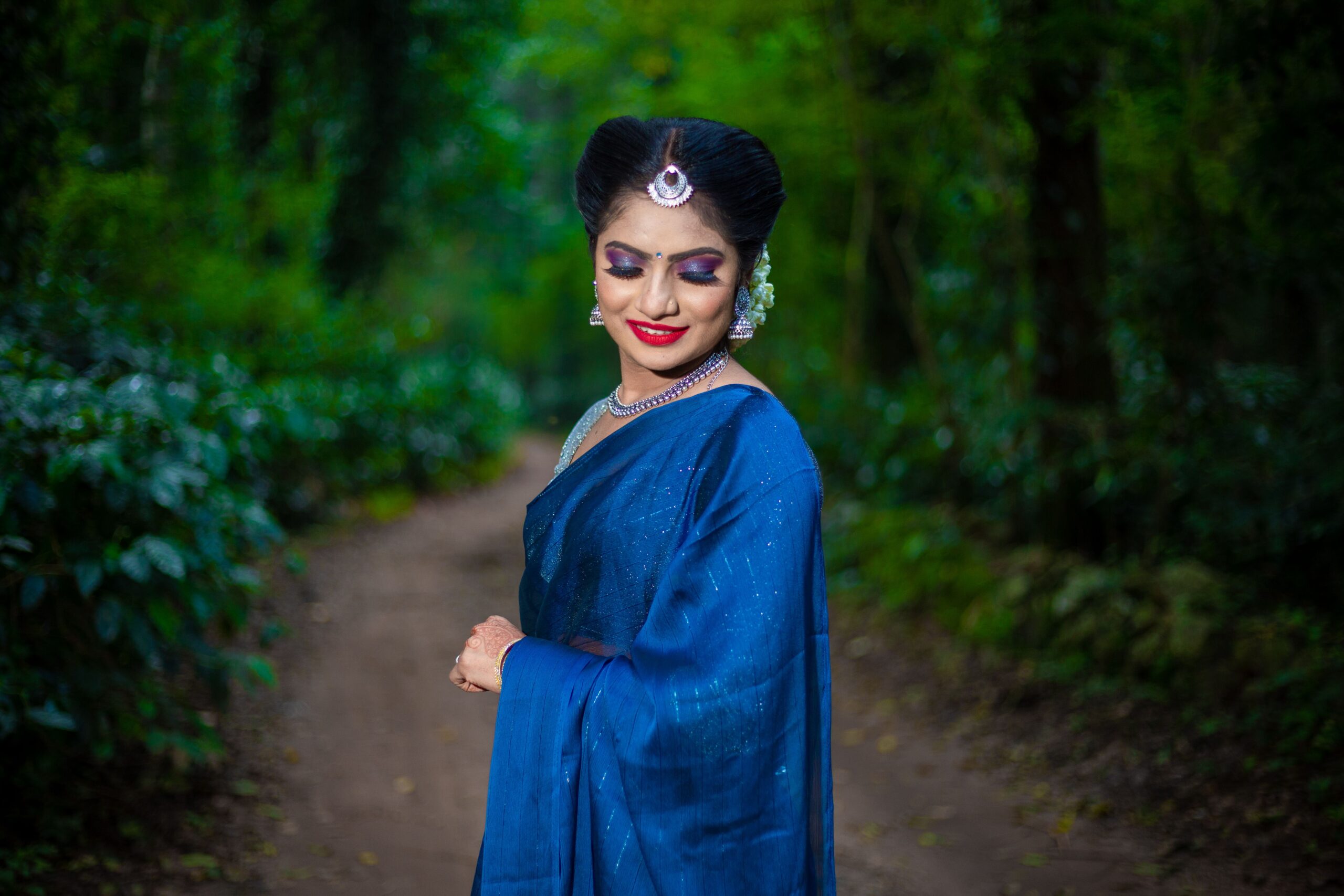 pexels photo 29805066 29805066 Woman in traditional blue saree standing gracefully amidst a vibrant green forest.