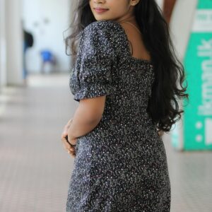 A young woman poses indoors in a floral dress, exuding confidence and elegance.